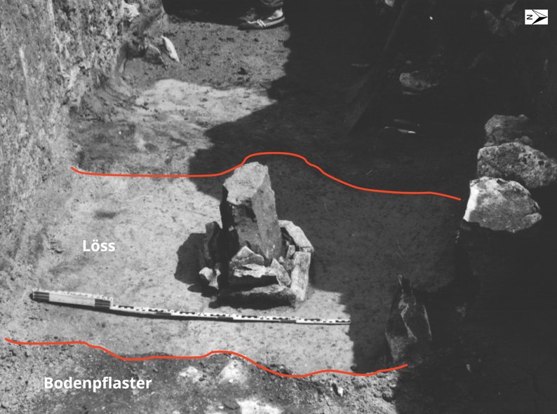 View of the stele from the east. The red lines mark the boundaries of features between the paved floor, the light-coloured loess loam, and a darker earthen feature adjoining it to the west. © LDA.