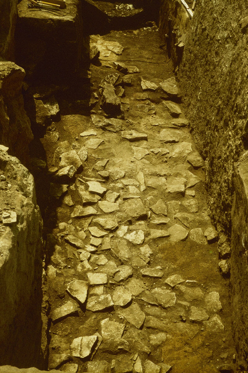 View on to the top layer of the slab paving within the burial chamber. Photo taken from the west. The small red sandstone stele is visible in the background. © LDA.